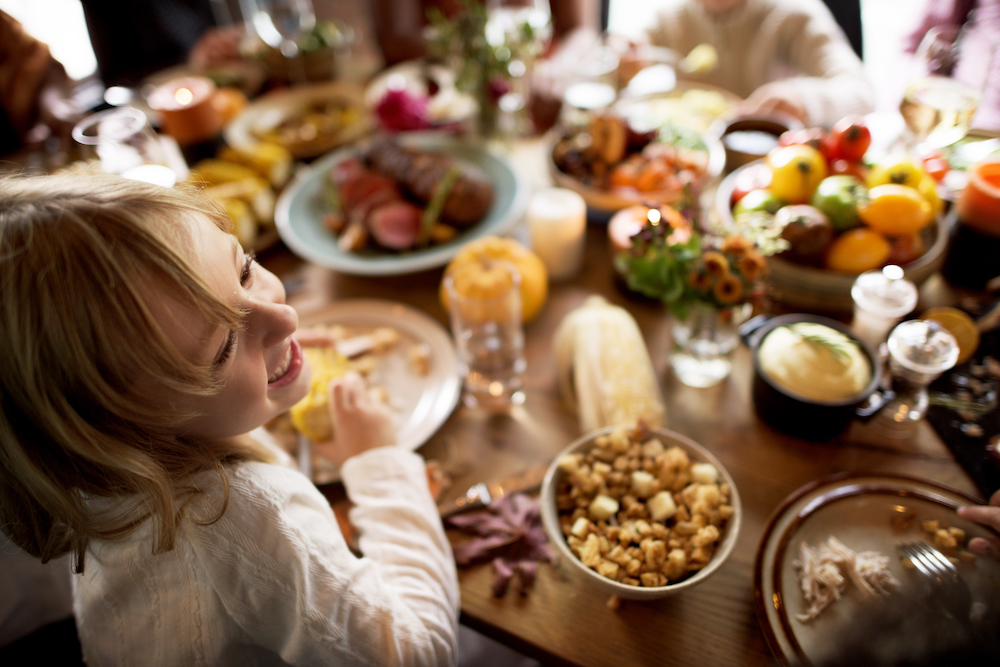 little girl in foreground eating thanksgiving at table with family in background for Healthy Living Germ-X Blog